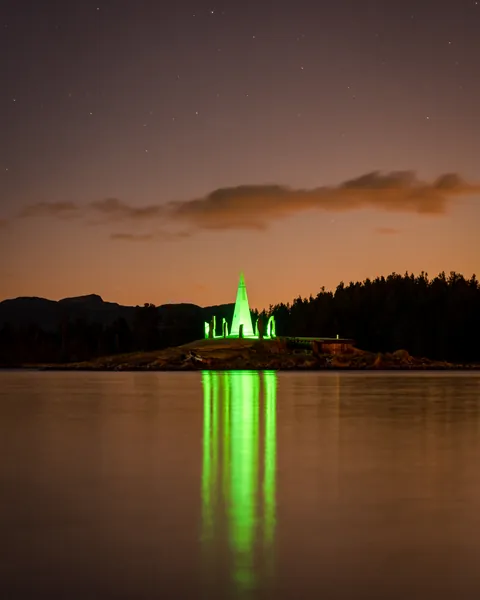 Solspeilet illuminated in green, reflected in the water at night